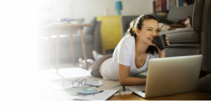 Personal Savings image: Young college age girl reclining on the floor drinking coffee while working on her computer